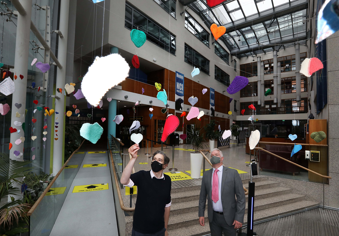 Minister Simon Harris DFHERIS with NCI Director of Marketing Robert Ward in the atrium of the College, admiring a 'yarn bomb' of handcrafted hearts