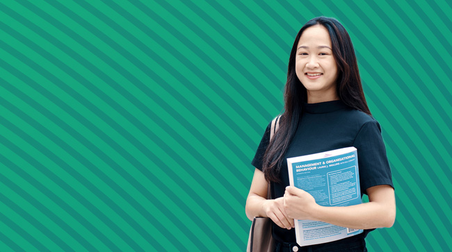 NCI student holding a textbook outside college campus entrance