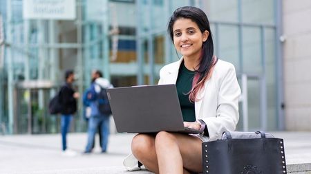 Student sitting on steps outside NCI campus with laptop on her lap