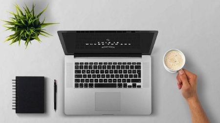 Laptop on a desk with a cup of coffee beside it