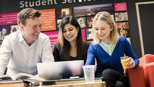 Three NCI students working on a laptop outside NCI Student Services office