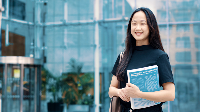 NCI student holding a textbook outside college campus entrance