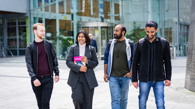 Four NCI students walking and talking to each other outside college campus entrance