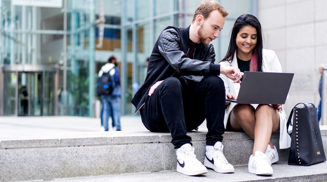 NCI students sitting on steps outside college, working on a laptop